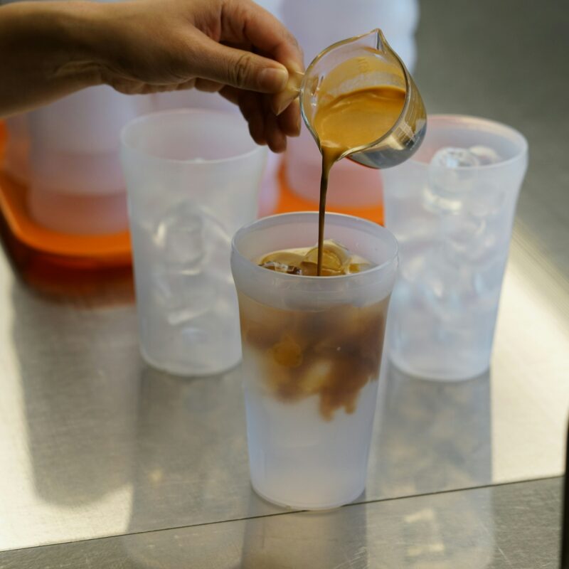 Une personne sert du café dans trois gobelets en plastique réutilisables.