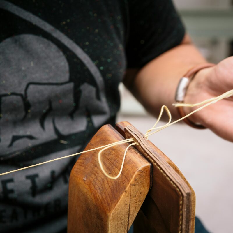 une personne cousant du cuir pour créer un sac, mettant en valeur l'artisanat et le savoir-faire.
