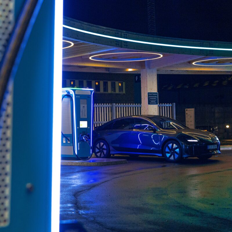 Voiture électrique connectée à une borne de recharge alimentée par des panneaux photovoltaïques, éclairée dans la nuit.